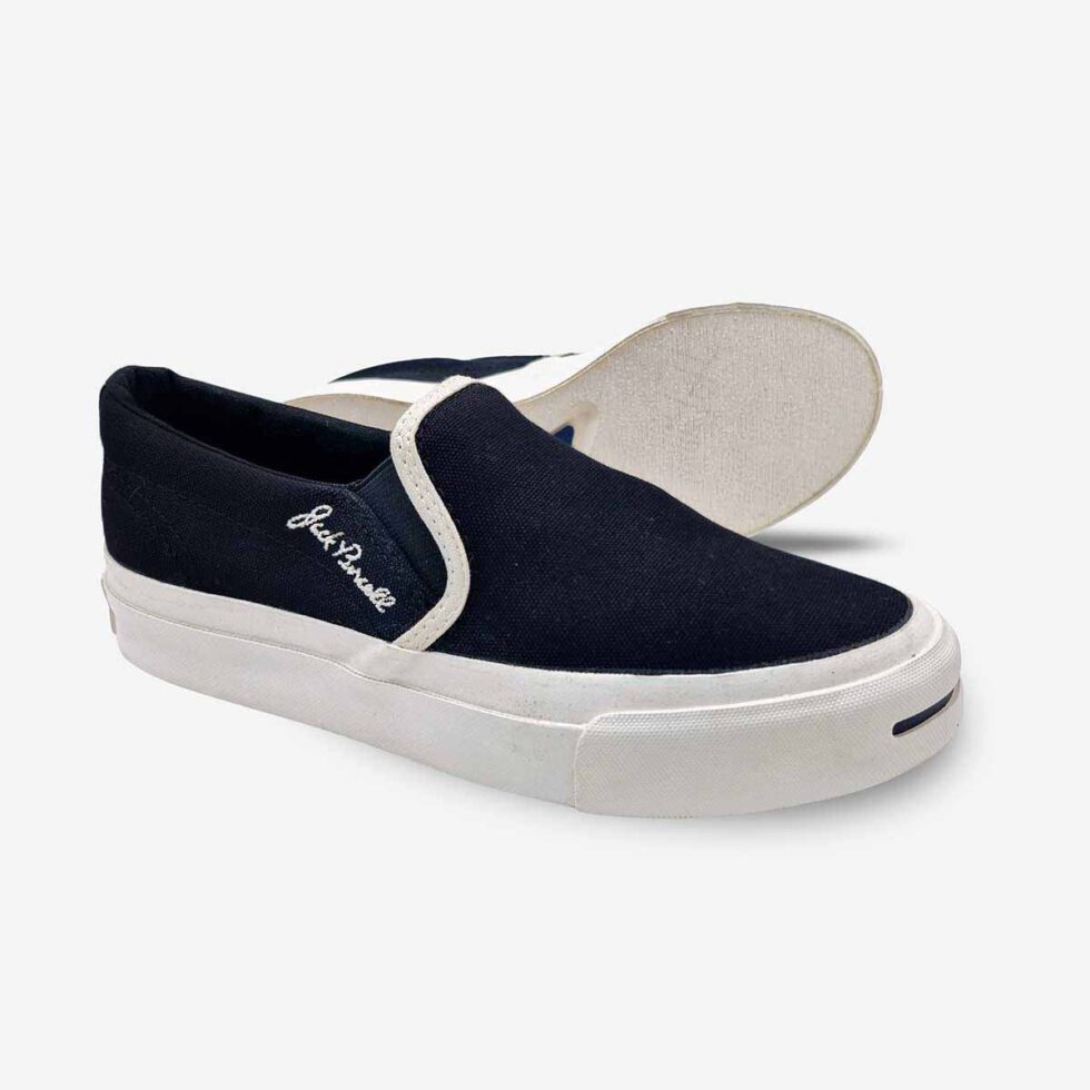 Angled view of Jack Purcell youth black slip-on sneakers showing textured rubber sole